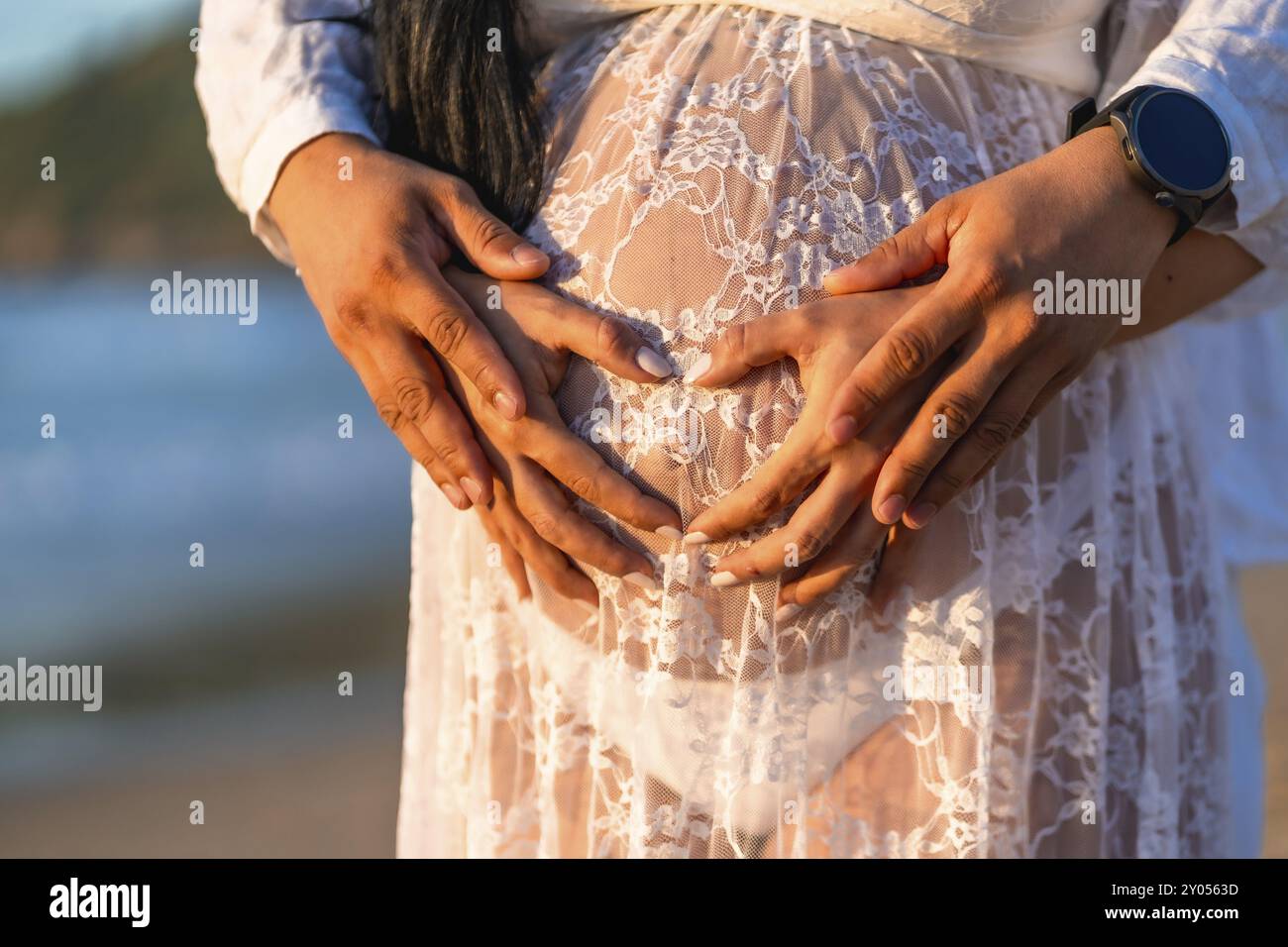 Eine schwangere Frau hält ihren Bauch mit ihren Händen, und ein Mann hält ihre Hände. Das Konzept der Liebe und Unterstützung der Schwangeren Stockfoto