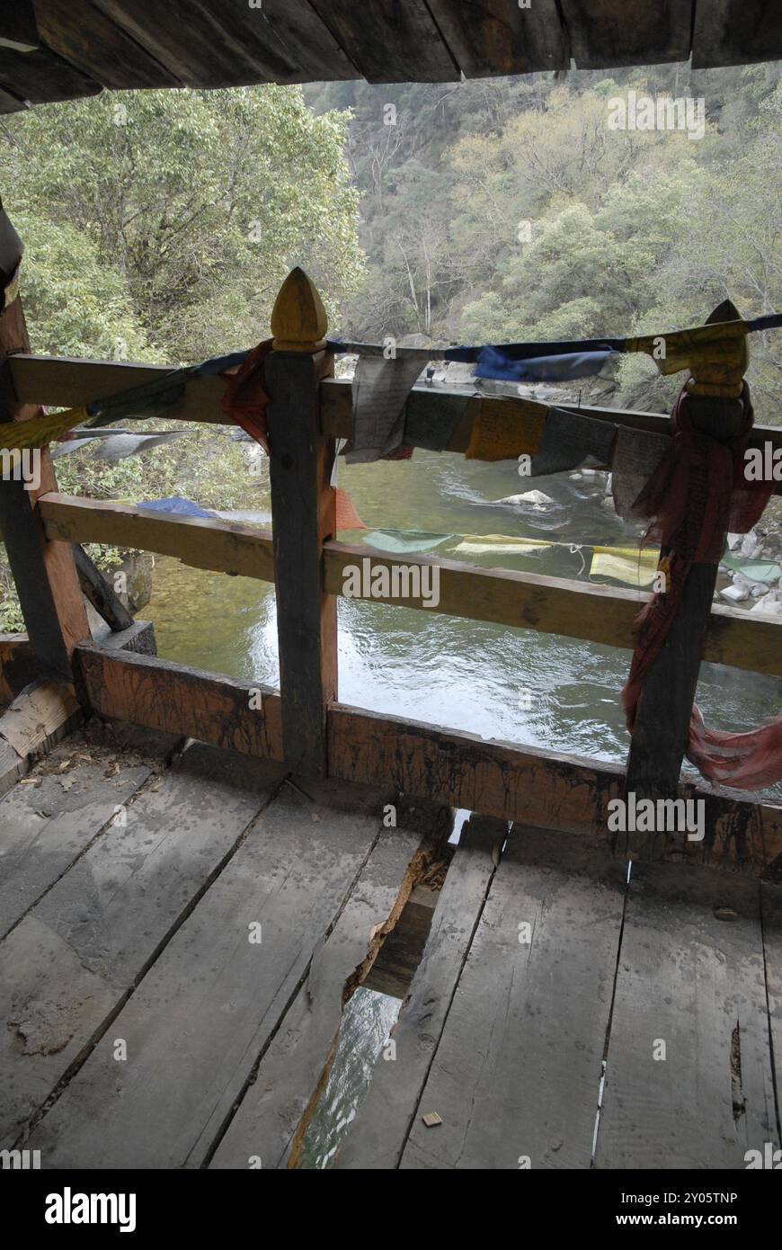 Verfaulte Fußgängerbrücke mit Gebetsfahnen über dem Fluss Stockfoto