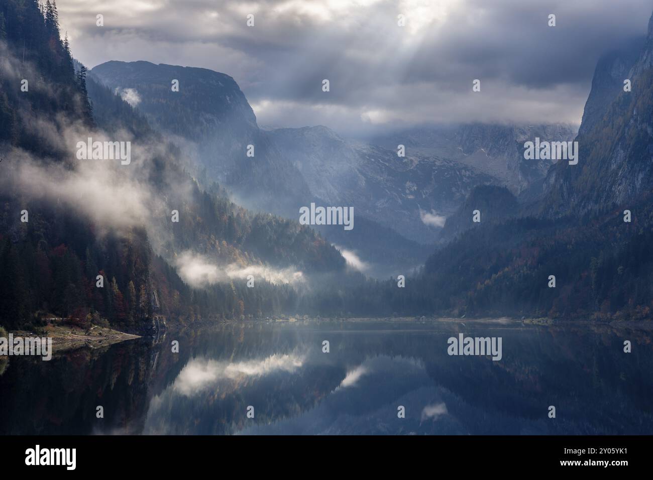 Der vordere Gosausee im Herbst. Der Dachstein in Wolken. Sonnenstrahlen strahlen strahlen durch die Wolken. Der Wald ist in Wolken gehüllt. Vorderer Gosausee, Gosa Stockfoto