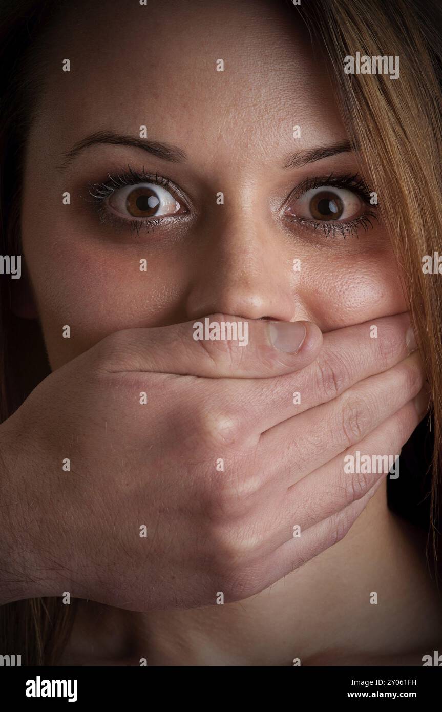 Nahaufnahme einer Hand, die einen Frauenmund bedeckt. Konzept häuslicher Gewalt oder Entführung. Dunkle Stimmung Stockfoto