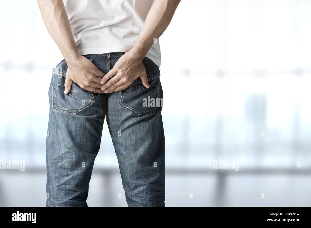 Ein Mann, der seinen Hintern vor Schmerzen in blauem Hintergrund hält Stockfoto