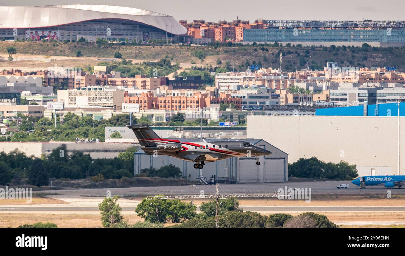 Madrid, Spanien; 18.05.2024: Auffälliges grau-rotes Privatflugzeug des Pilatus PC-24-Modells beginnt vor der Fußballstühle zu landen Stockfoto