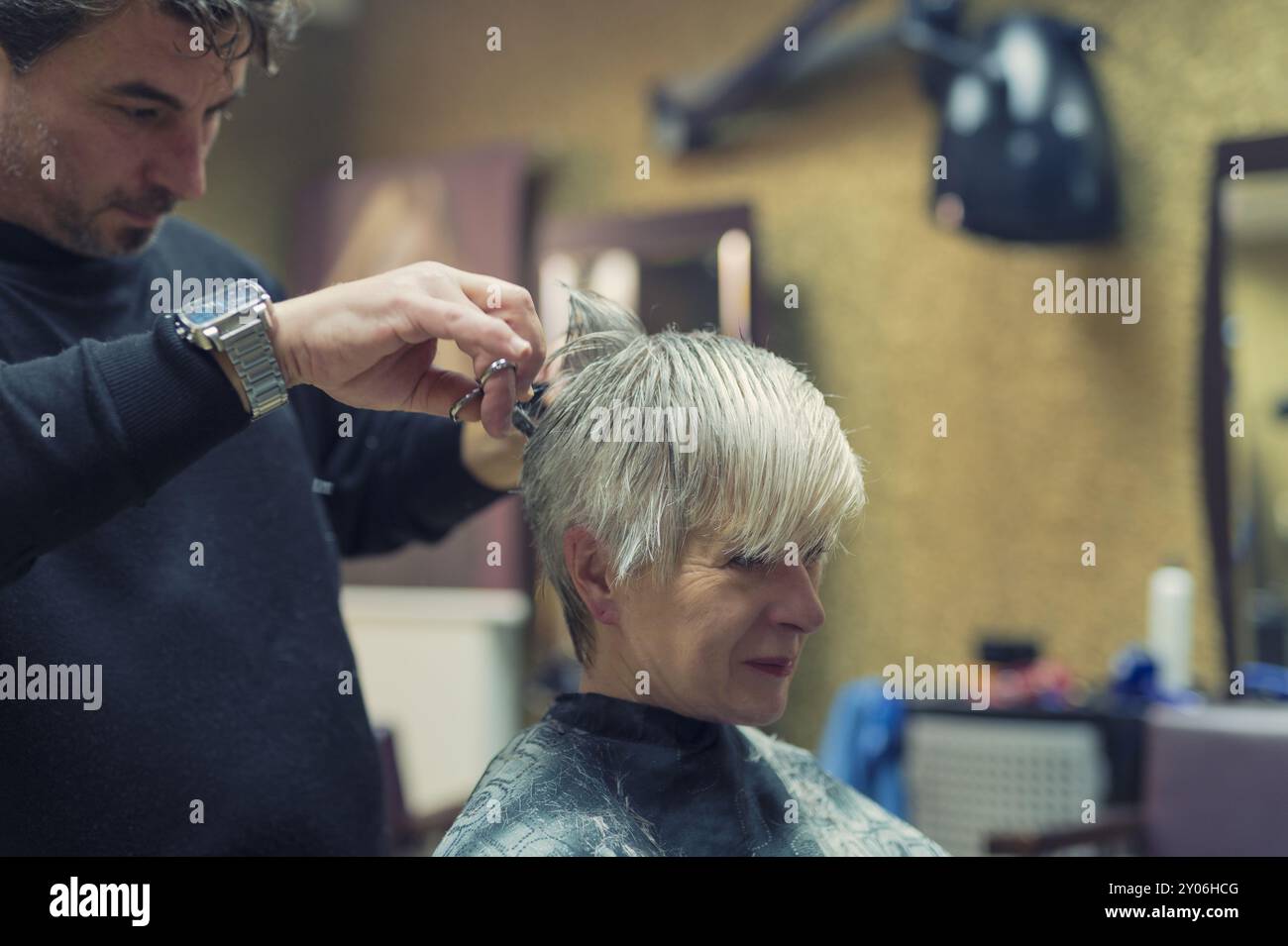 Ein Friseur schneidet die Haare am Hinterkopf einer Seniorin Stockfoto