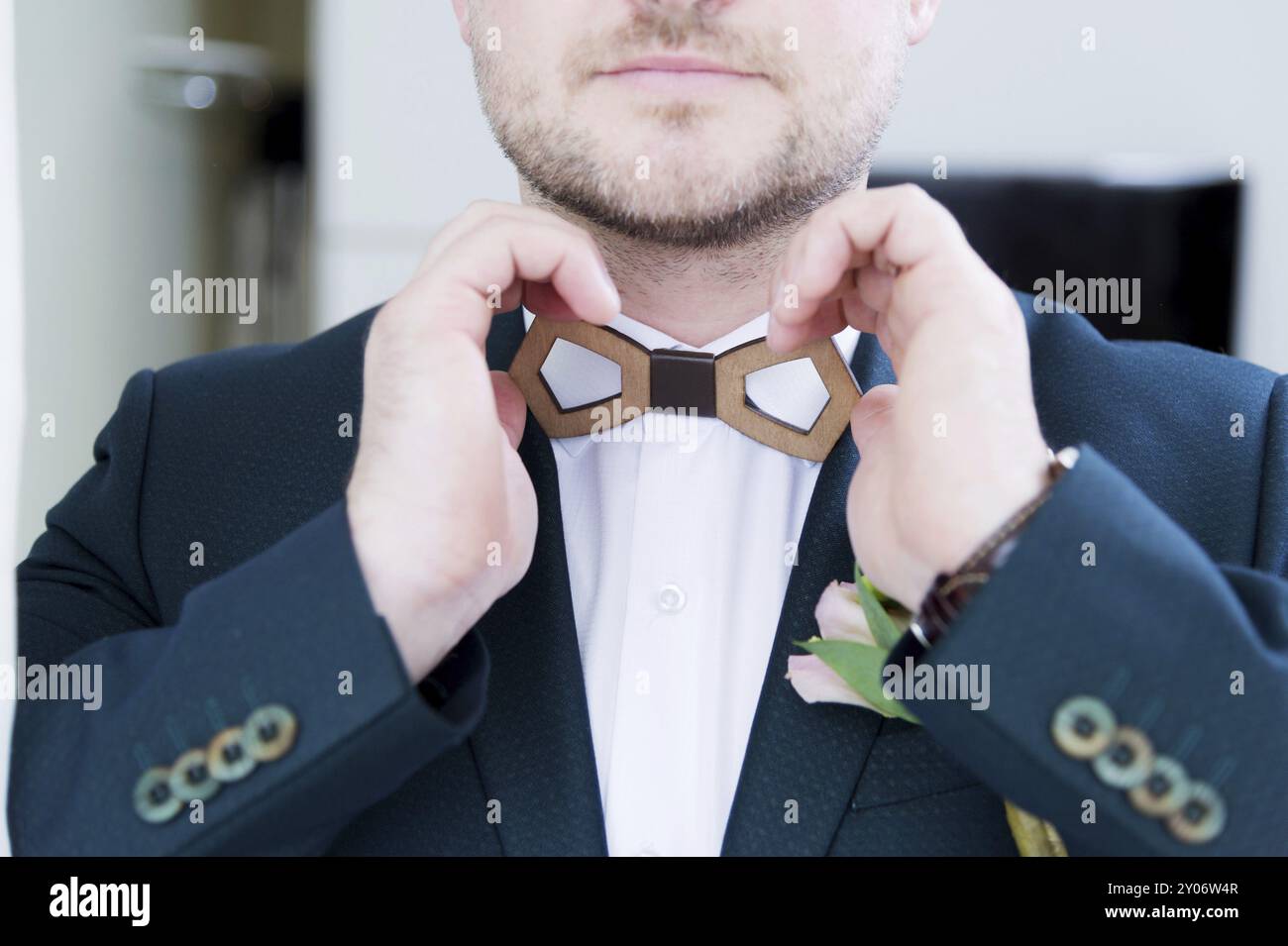 Ein festes Brautpaar mit Bart im Anzug passt die hölzerne Schleife am Kragen mit seinem weißen Hemd an. Super Nahaufnahme. Das Konzept des Geschäftsstils Stockfoto