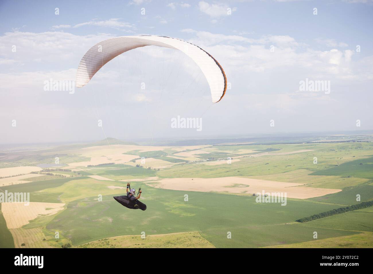 Professioneller Gleitschirm im Kokon-Anzug fliegt hoch über dem Boden gegen den Himmel und die Felder Stockfoto