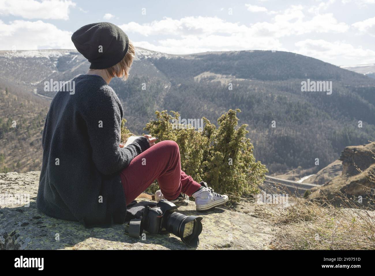 Porträt eines Hipster-Designers Fotografin mit Hut und Sonnenbrille zeichnet ein Pastellpapier in ihr Notizbuch, das draußen auf einem Felsen in den Bergen sitzt. Die Stockfoto