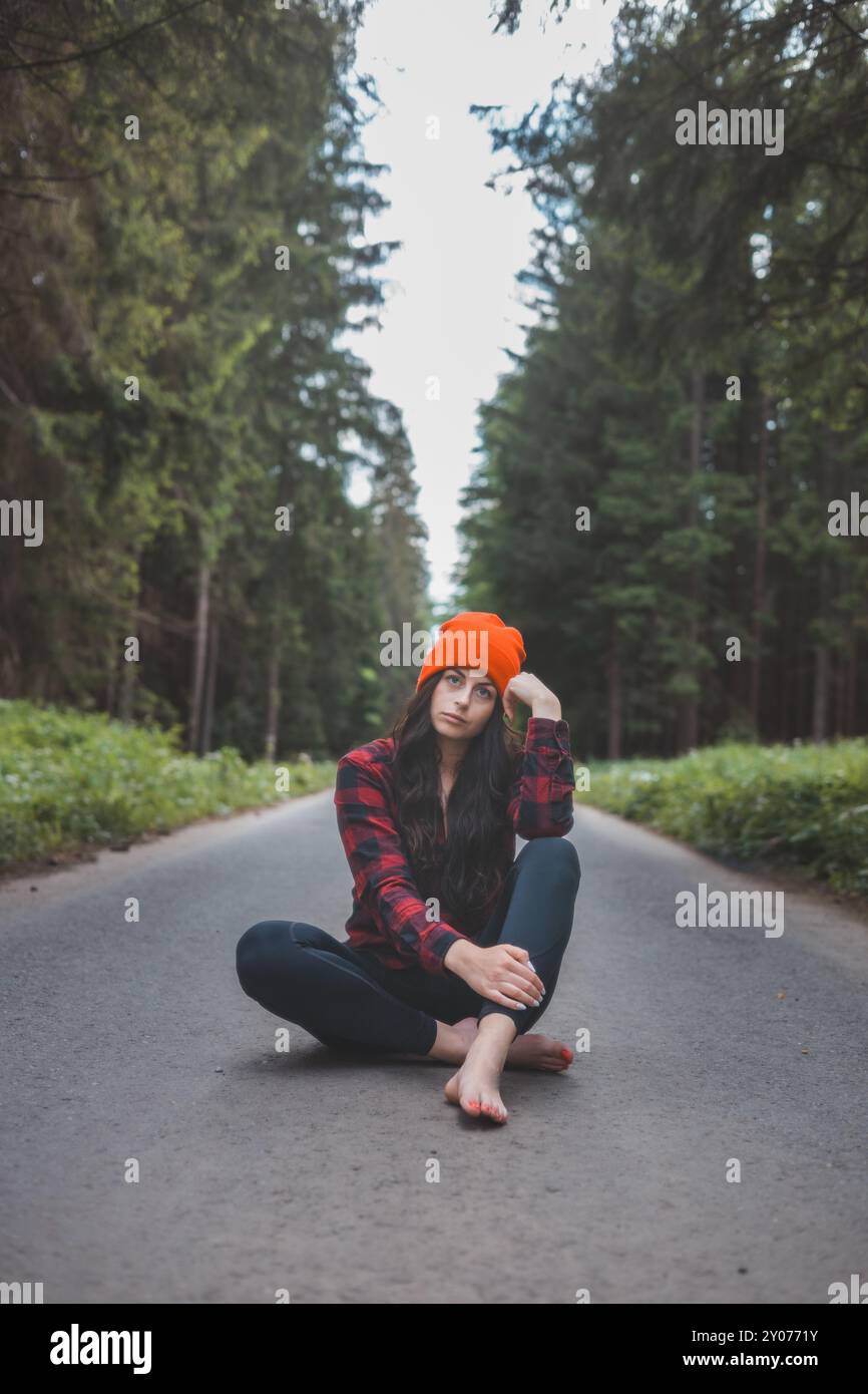 Charmante Brünette, die auf einem Pfad inmitten der wilden Natur sitzt und das Gefühl von Freiheit und frischer Luft genießt. Üppiges Grün und hohe Bäume, Symbol Stockfoto