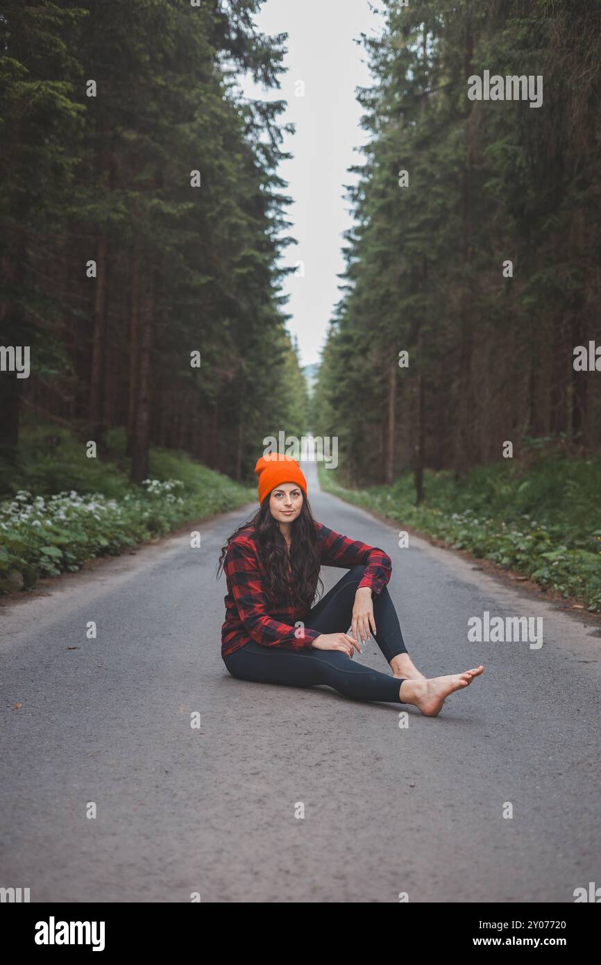 Charmante Brünette, die auf einem Pfad inmitten der wilden Natur sitzt und das Gefühl von Freiheit und frischer Luft genießt. Üppiges Grün und hohe Bäume, Symbol Stockfoto