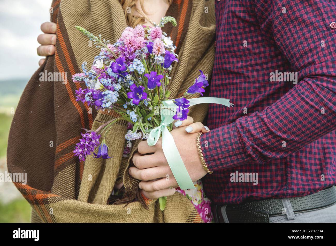 Nahaufnahme einer Hand, die ein Paar Mann und seine Freundin mit Blumenstrauß umschließt. Kariertes Hemd und Strickpullover Stockfoto