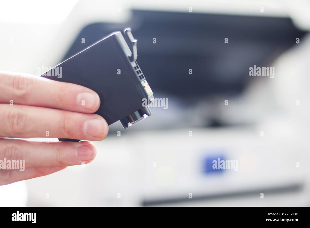 Druckerpatrone eines Drittanbieters in der Hand, Drucker im unscharfen Hintergrund Stockfoto