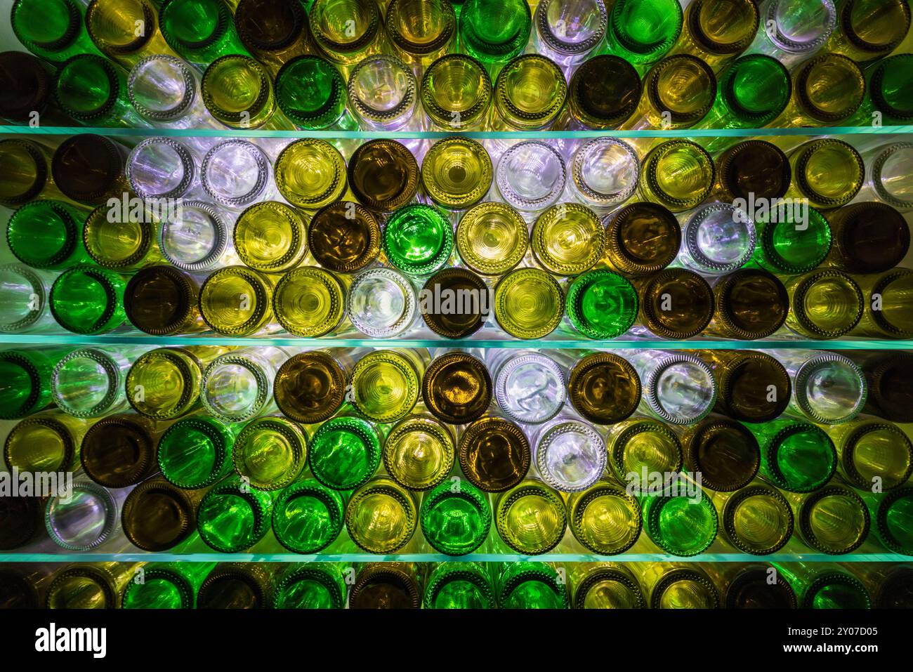 Natürlich beleuchtete, mehrfarbige Weinflaschen auf Glasregalen Stockfoto