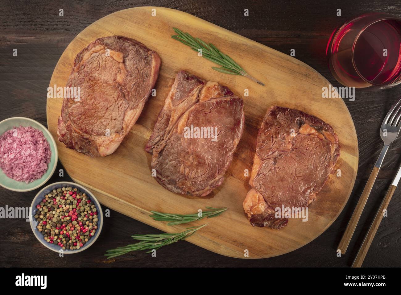 Rinderfilet Steaks, Schuß von der Oberseite in einem dunklen Holzmöbeln im Landhausstil Hintergrund mit Rosmarin, Salz, Pfeffer, und Wein Stockfoto