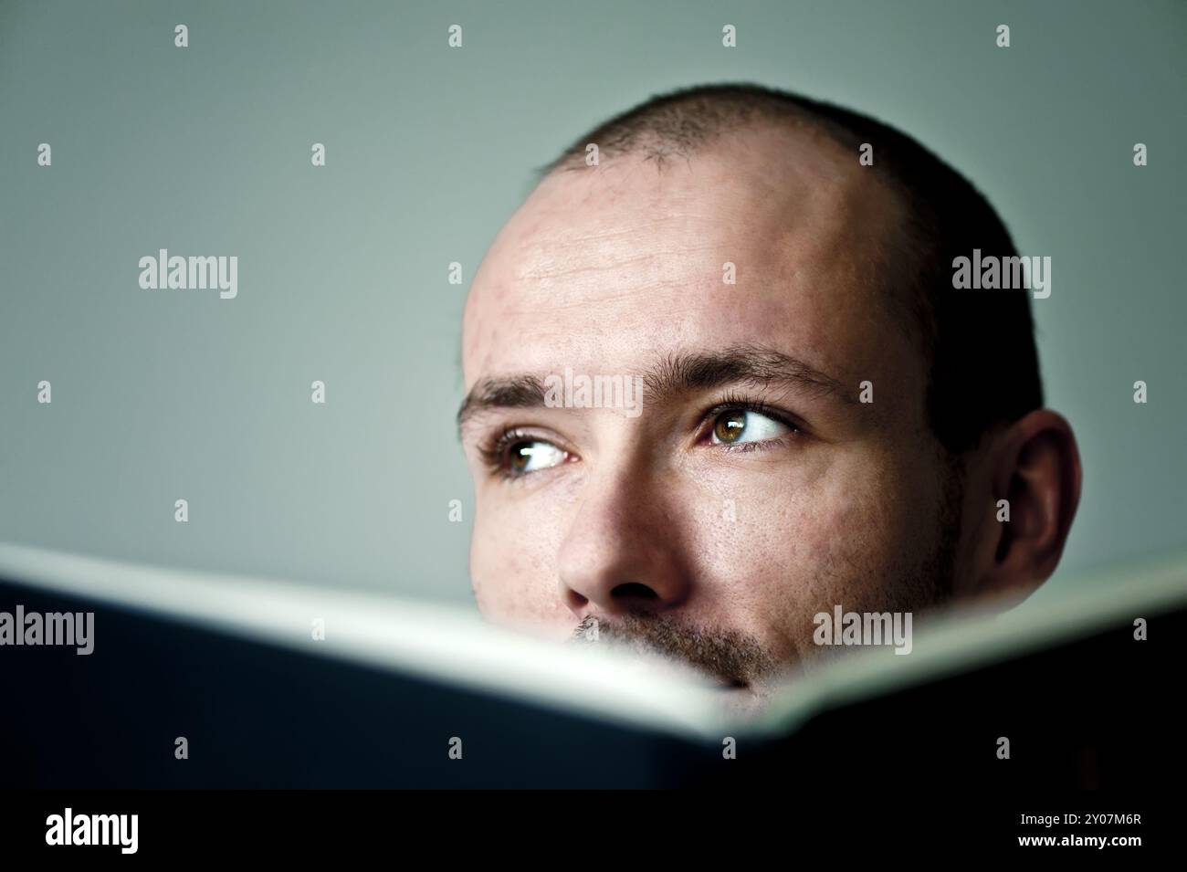 Der junge Mann schaut nachdenklich über den Rand eines Buches Stockfoto