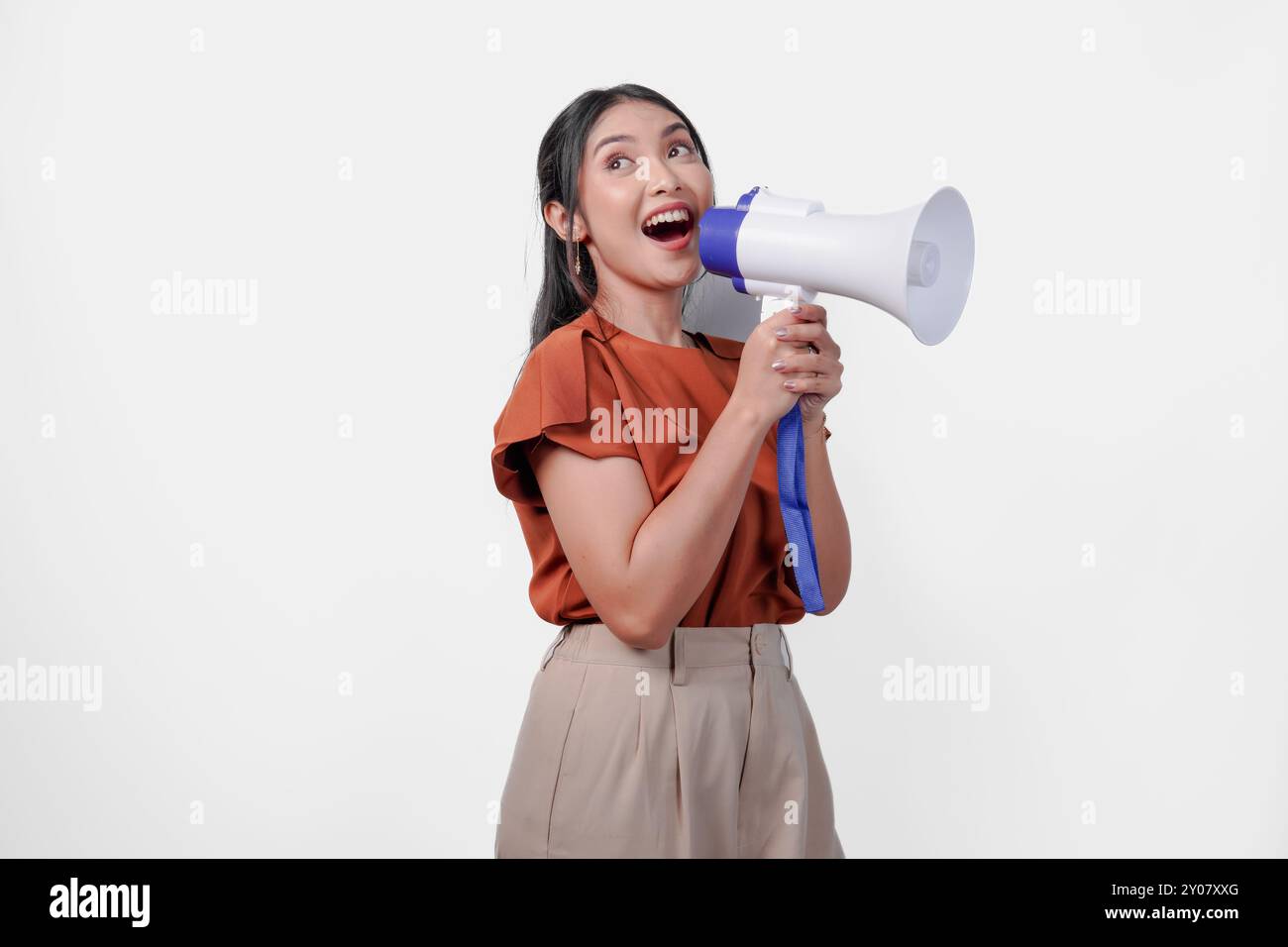 Die fröhliche junge asiatische Frau hält ein Mikrofon und macht ein lautes Geräusch. Sie lächelt und ist glücklich. Stockfoto