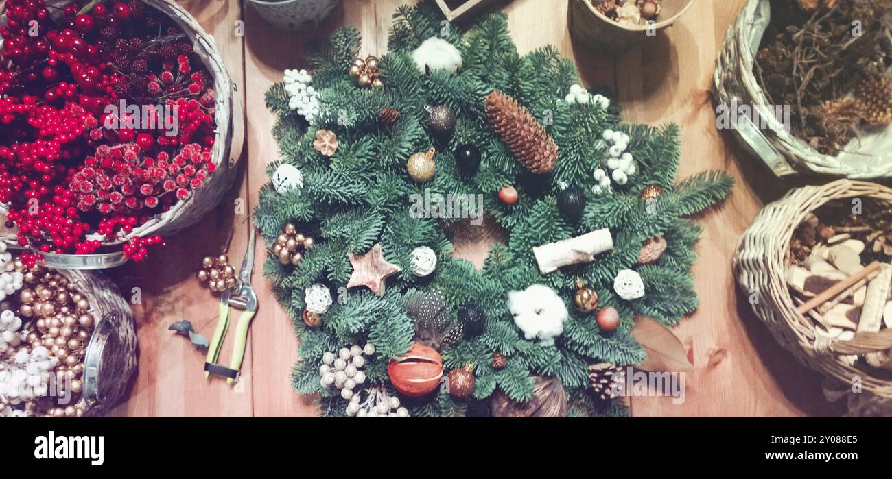 Blick von oben auf den dekorierten Weihnachtskranz aus grüner Tanne auf Holztisch mit Körben aus roten Beeren und Designelementen Stockfoto
