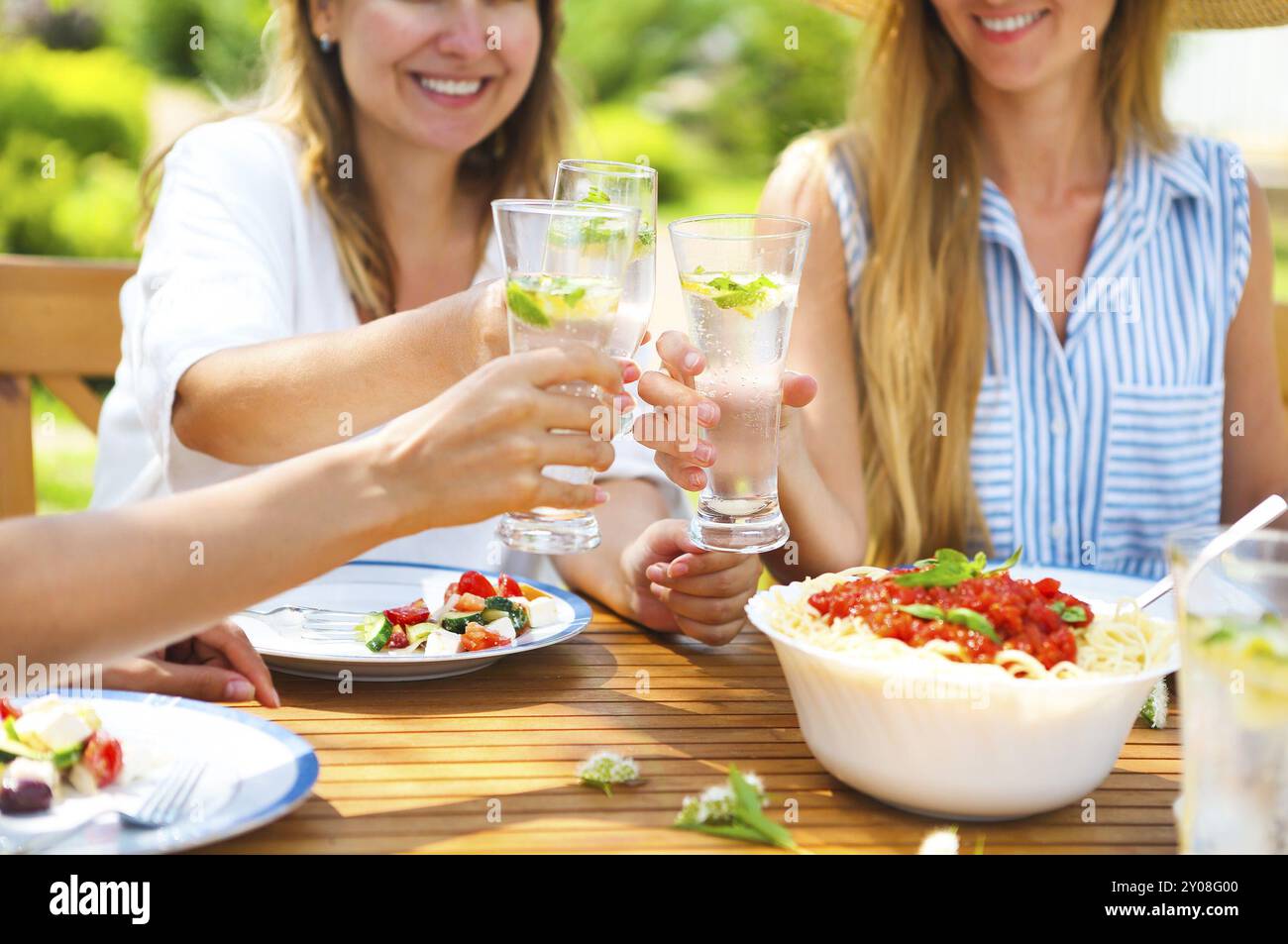 Glücklich Freundinnen mit Gläsern Limonade am Esstisch im Rasen. Nahaufnahme Stockfoto