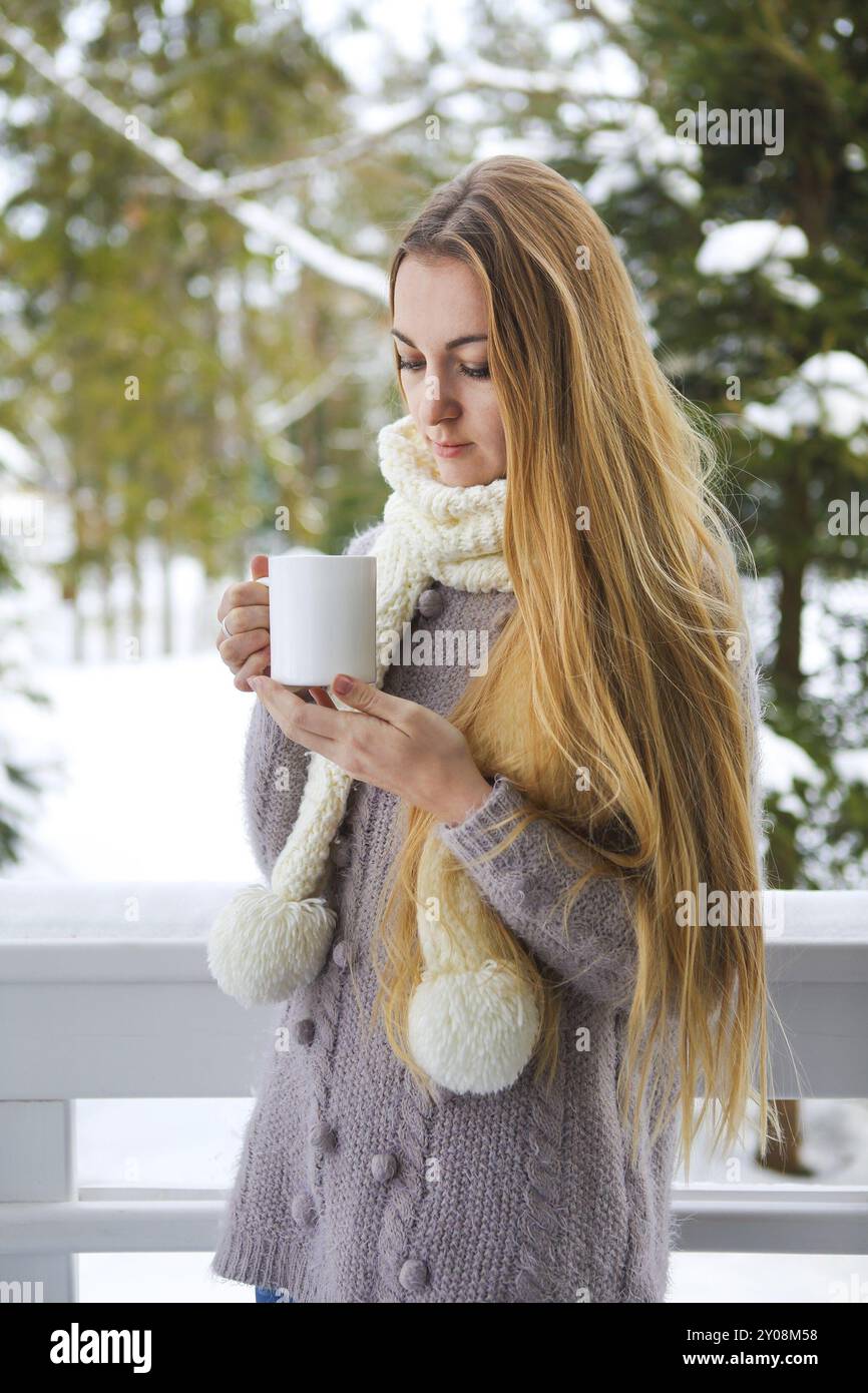 Junge schöne Frau mit blondem Haar draußen mit einer Tasse heißem Kaffee, der gestrickte warme Pullover trägt. Winter Confort Konzept Stockfoto