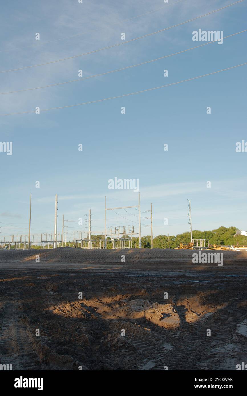 Vertikale Ansicht bei Sonnenuntergang der elektrischen Umspannstation mit Hochspannungsleitungen in St. Petersburg, Florida. Blick auf Schmutz, temporäre Silt Fechten, grüne Gras Stockfoto