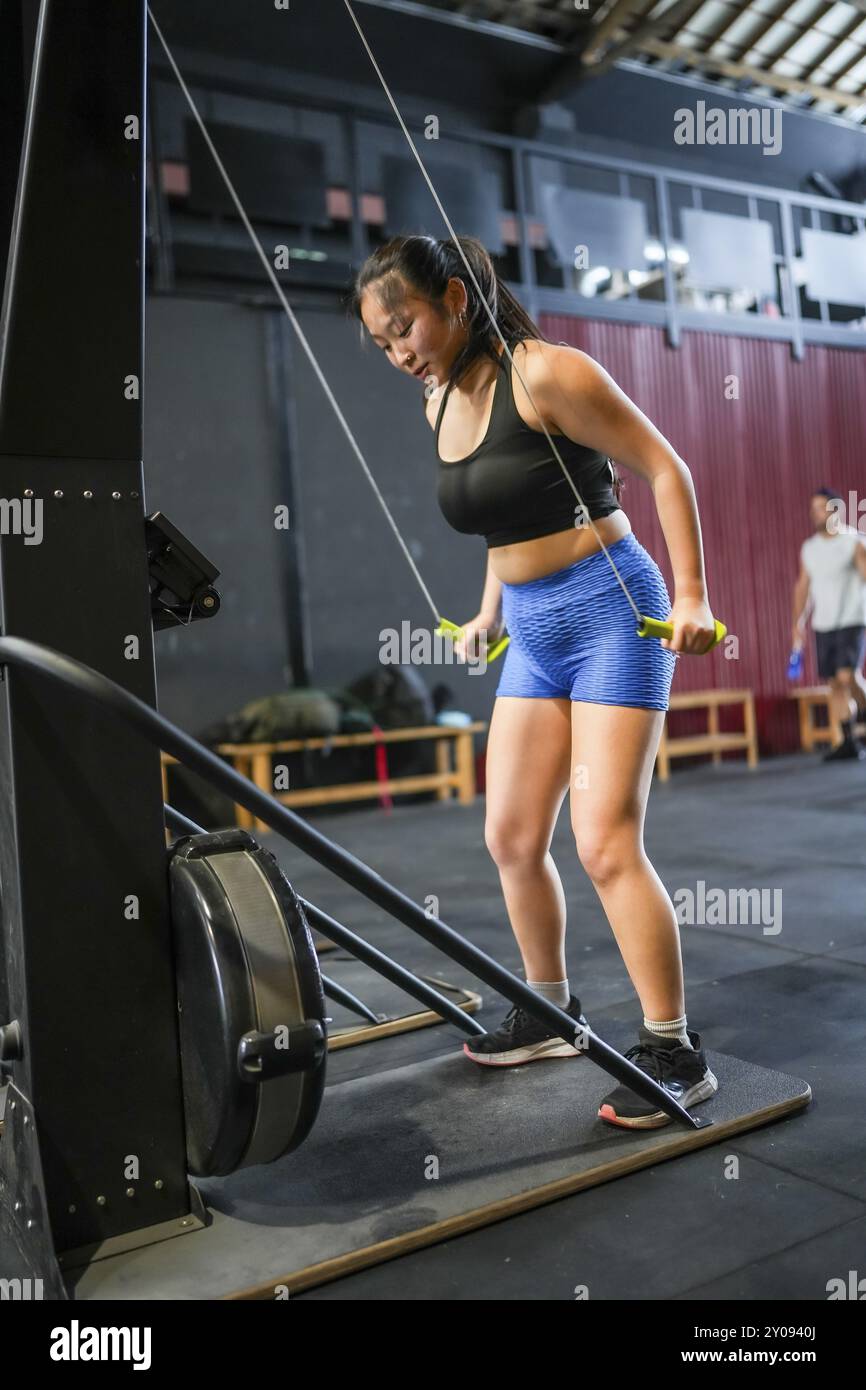 Vertikales Foto in voller Länge von einer asiatischen Frau, die in einem Fitnessstudio mit einem Pulldown-Lat-Gerät trainiert Stockfoto