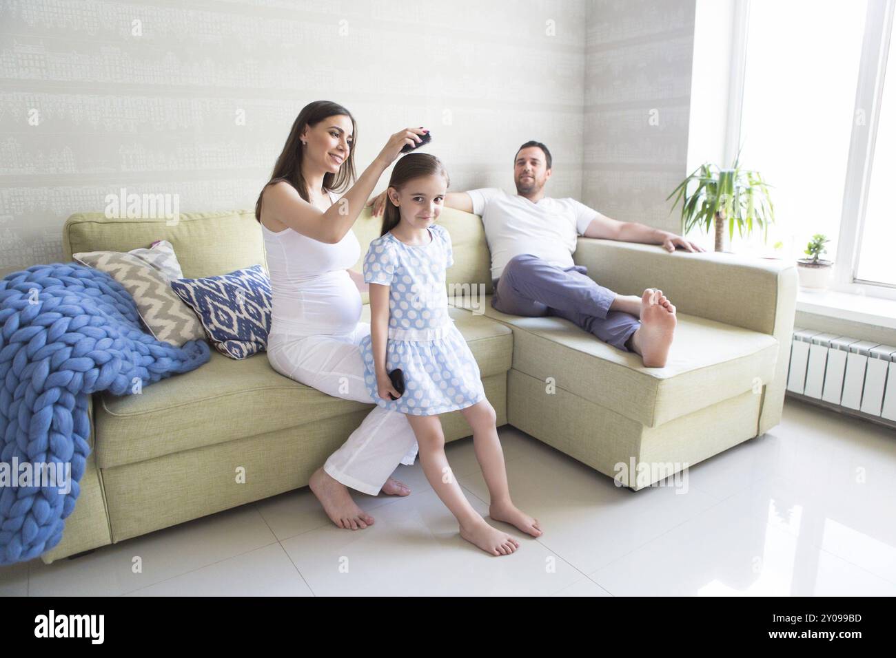 Adorable junge schwangere Familie im Wohnzimmer. Die Mutter ihre Tochter die Haare kämmen. Glück und Liebe Konzept Stockfoto