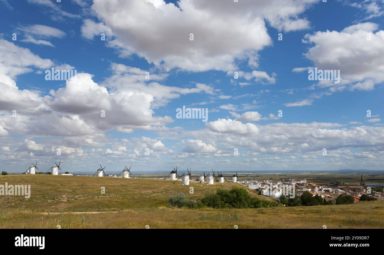 Weite Landschaft mit Windmühlen und einem Dorf im Hintergrund. Der Himmel ist blau mit vielen weißen Wolken und die Umgebung ist grün und weitläufig, wi Stockfoto