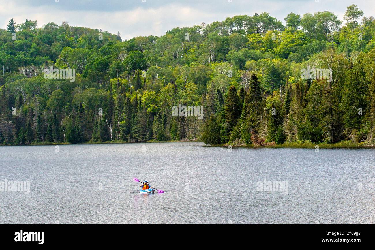 Eine Person, die mit einem Kajak über den Mink Lake im Cook County im Norden von Minnesota paddelt, mit dem Superior National Forest im Hintergrund. Stockfoto
