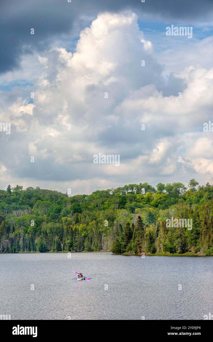 Eine Person, die mit einem Kajak über den Mink Lake im Cook County im Norden von Minnesota paddelt, mit dem Superior National Forest im Hintergrund. Stockfoto