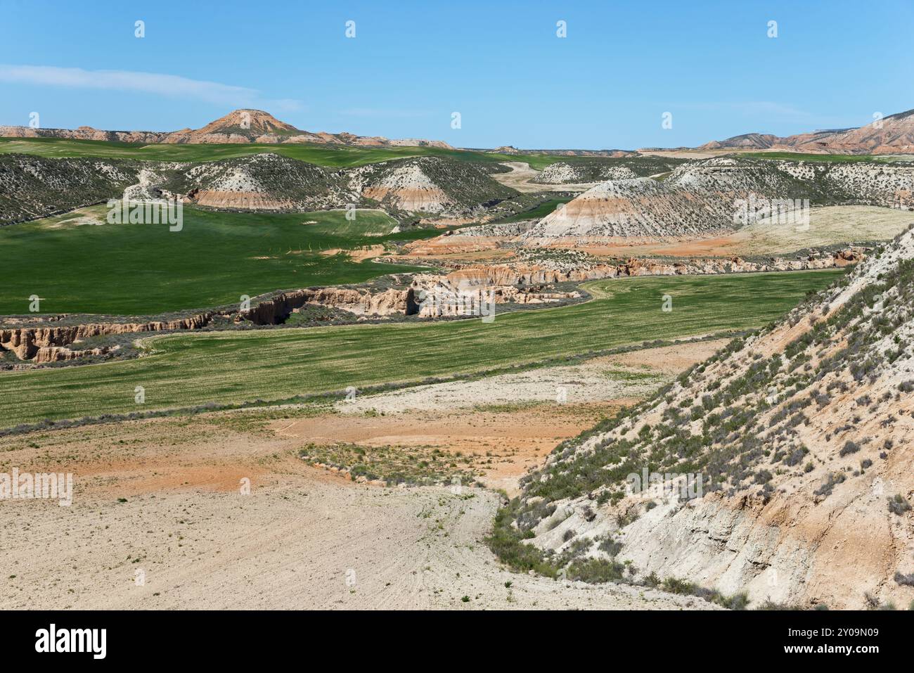 Grüne Felder und trockene Hügel unter azurblauem Himmel in einer weiten Landschaft, Bardenas Reales Naturpark, Bardena Negra, Wüste, Halbwüste, Navarra, Naf Stockfoto