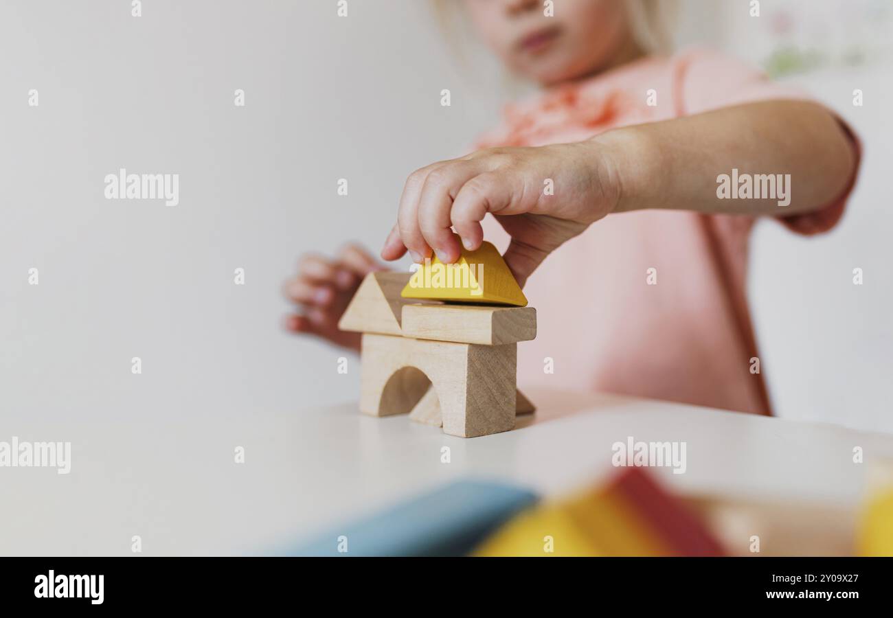 Kleines Mädchen, das zu Hause oder im Kindergarten Holzbausteine spielt. Entwicklungs- und Baukonzept. Mehrfarbige Lernsteine für e Stockfoto