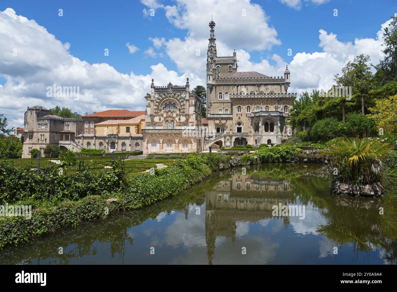 Historisches Schloss mit reflektiertem Bild im See, umgeben von Baeumen und bewoelktem Himmel, Palacio Hotel do Bucaco, Mata Nacional do Bucaco, Natio Stockfoto