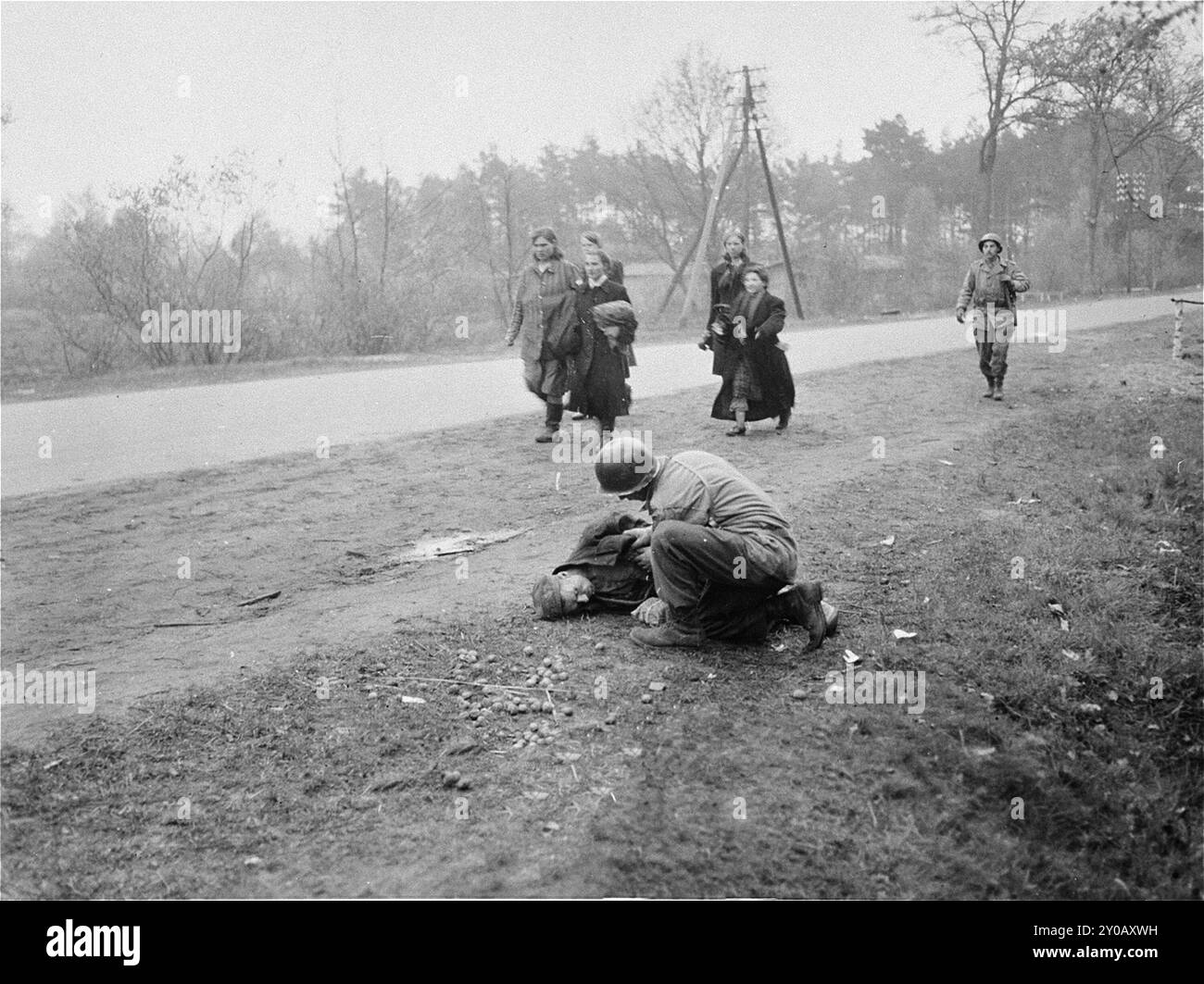 Polnischer Überlebender aus dem KZ Woebbelin, stirbt kurz nach seiner Befreiung am Straßenrand an Unterernährung. Ein US-Soldat versucht vergeblich, Hilfe für den Mann zu leisten, während im Hintergrund befreite polnische Frauen an Schuhen vorbeiziehen, die von einheimischen deutschen Frauen beschlagnahmt wurden. Die SS eröffnete Wöbbelin im Februar 1945, um KZ-Gefangene aufzunehmen, die die SS aus anderen Lagern evakuiert hatte, um ihre Befreiung durch die Alliierten zu verhindern. Das Lager wurde am 2. Mai 1945 freigelassen. Stockfoto