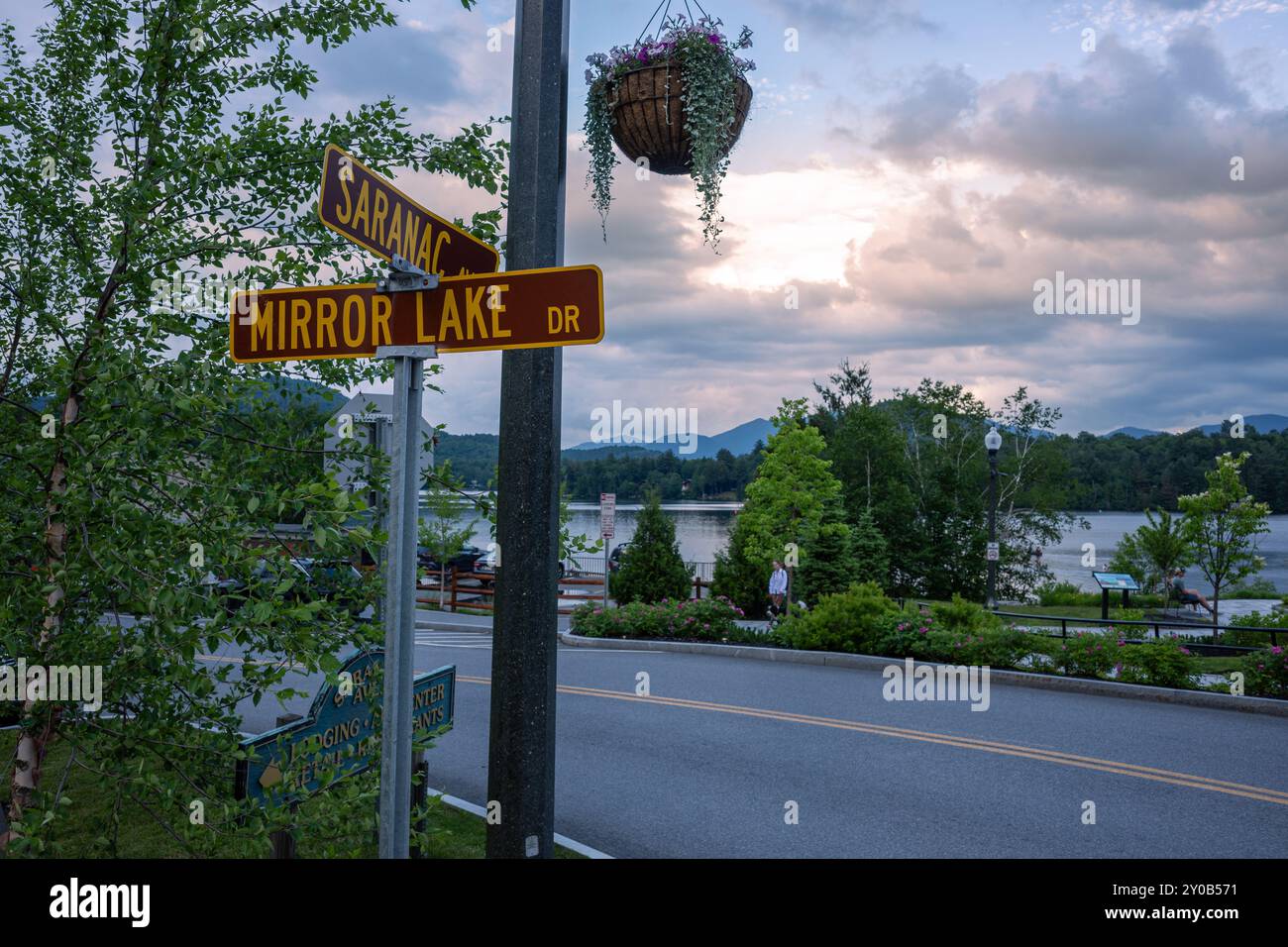 Erleben Sie die ruhige Schönheit eines Abends am Mirror Lake in Lake Placid, New York, wo die Straßenüberquerung in das warme Licht des Sonnenuntergangs getaucht ist Stockfoto