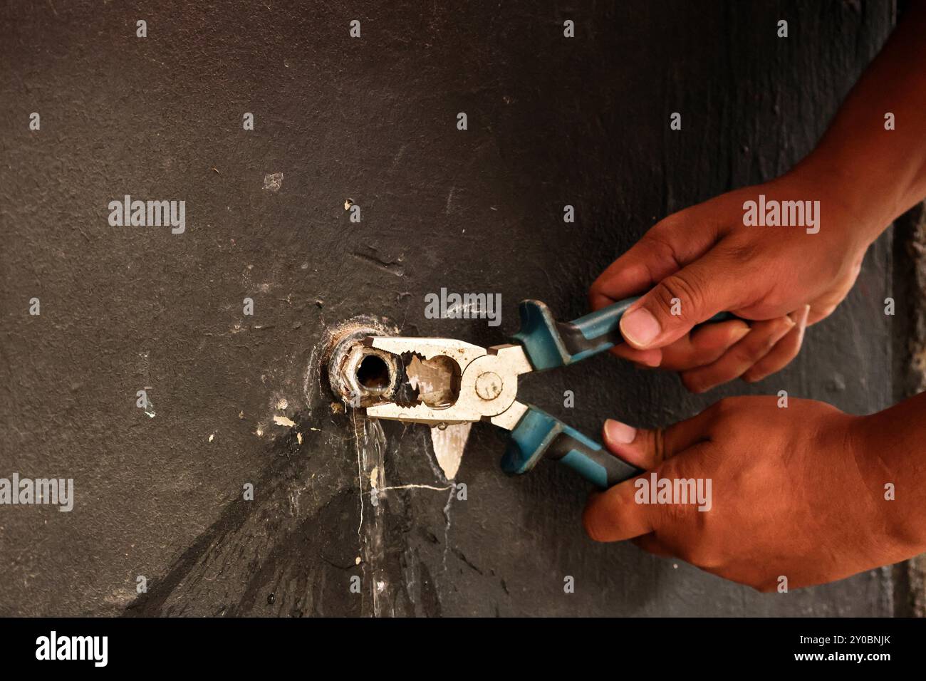 Hand eines asiatischen Klempners, der den Wasserhahn mit einer Zange an der Wand befestigt Stockfoto