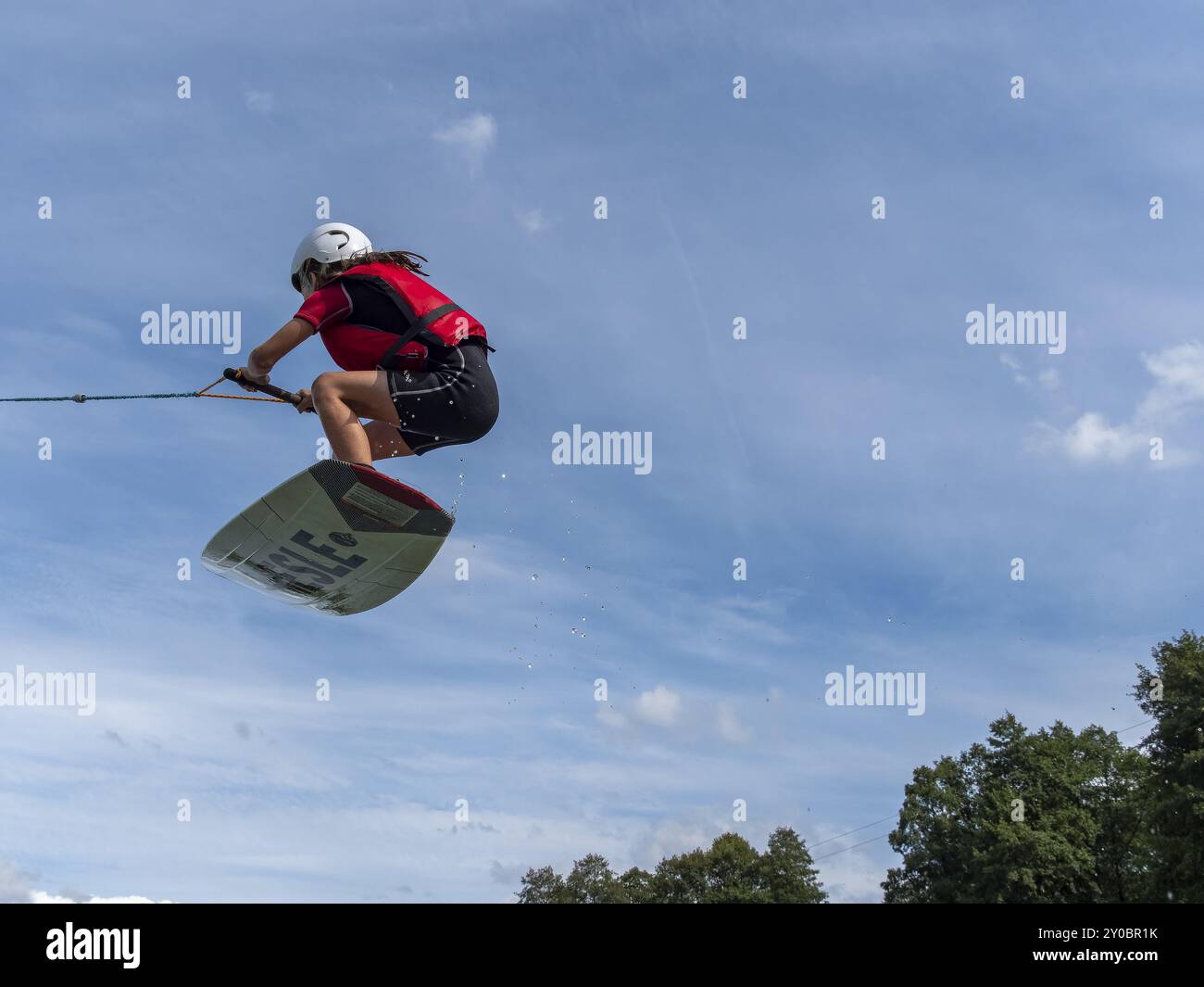 Junge oder Mädchen springen und fliegen mit Wakeboard, Wassersport und Wasserski im Wakepark Stockfoto