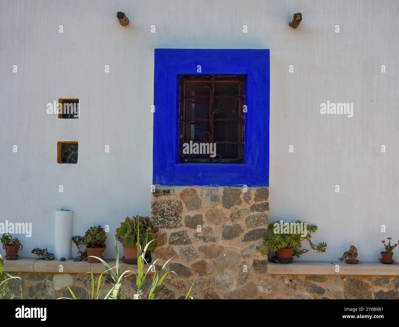 Traditionelle Fassade mit blauem Fensterrahmen und Topfpflanzen auf einer Steinmauer, ibiza, mittelmeer, spanien Stockfoto