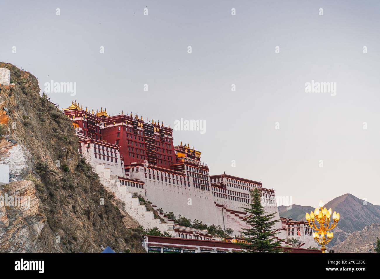Die abgewinkelte Front des Potala-Palastes wurde oben und die Straßenlandschaft unten unter einem klaren blauen Himmel während des frühen Abends in Lhasa, Tibet, angehoben. Horizontal Stockfoto