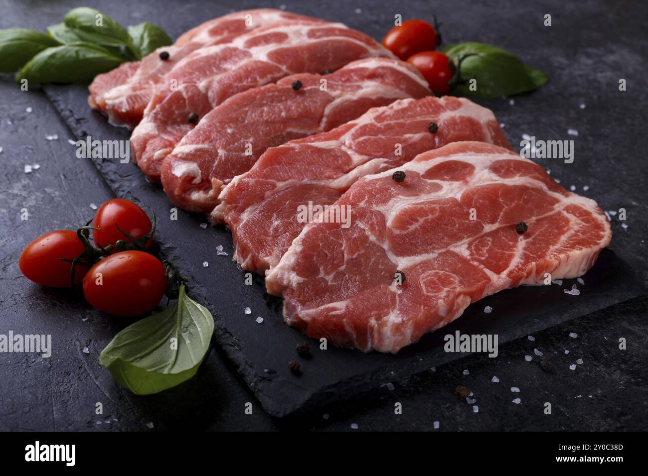 Scheiben Schweinerücken mit Kräutern, Salz und Pfeffer, Schwarzer Stein Hintergrund Nahaufnahme Stockfoto