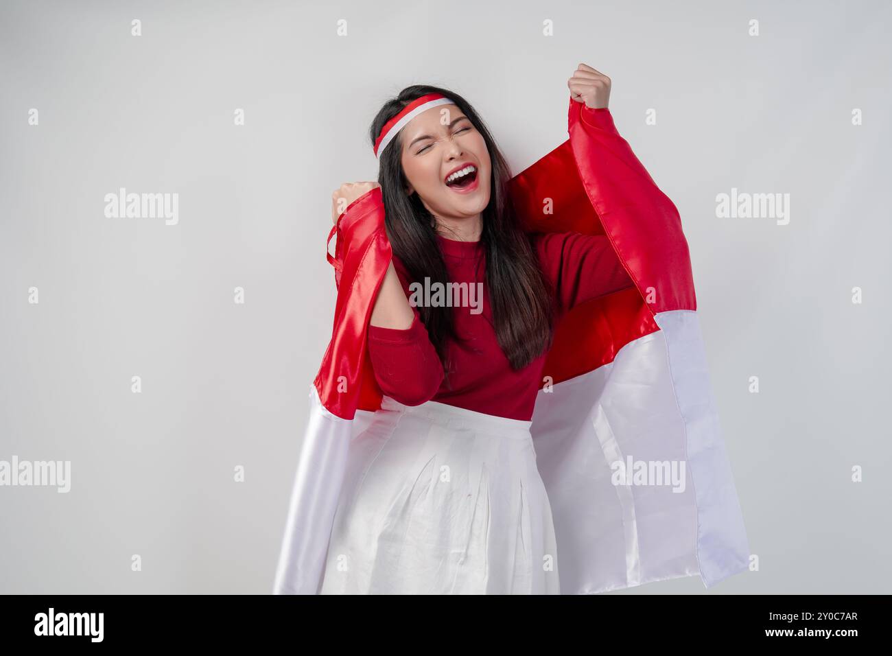 Fröhliche junge asiatische Frau hält indonesische Flagge auf dem Rücken und hebt mit glücklichem Erfolg Fäuste in die Luft. Indonesische Independen Stockfoto