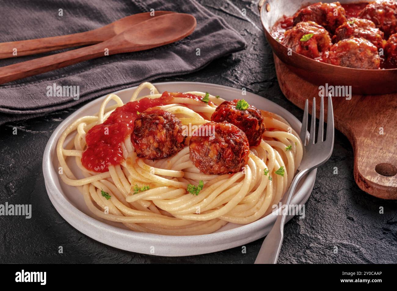 Fleischbällchen. Rindfleischbällchen, in einer Pfanne und mit einem Teller Spaghetti-Pasta, auf schwarzem Schiefergrund, italienische Küche Stockfoto