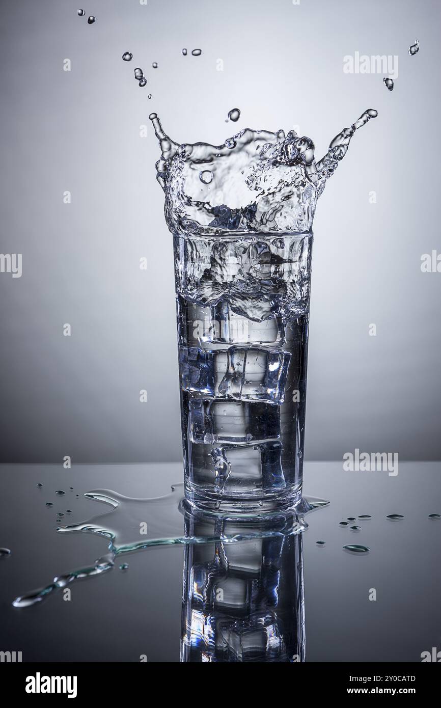 Eis wird in ein Glas Wasser geworfen, was einen Spritzer verursacht Stockfoto