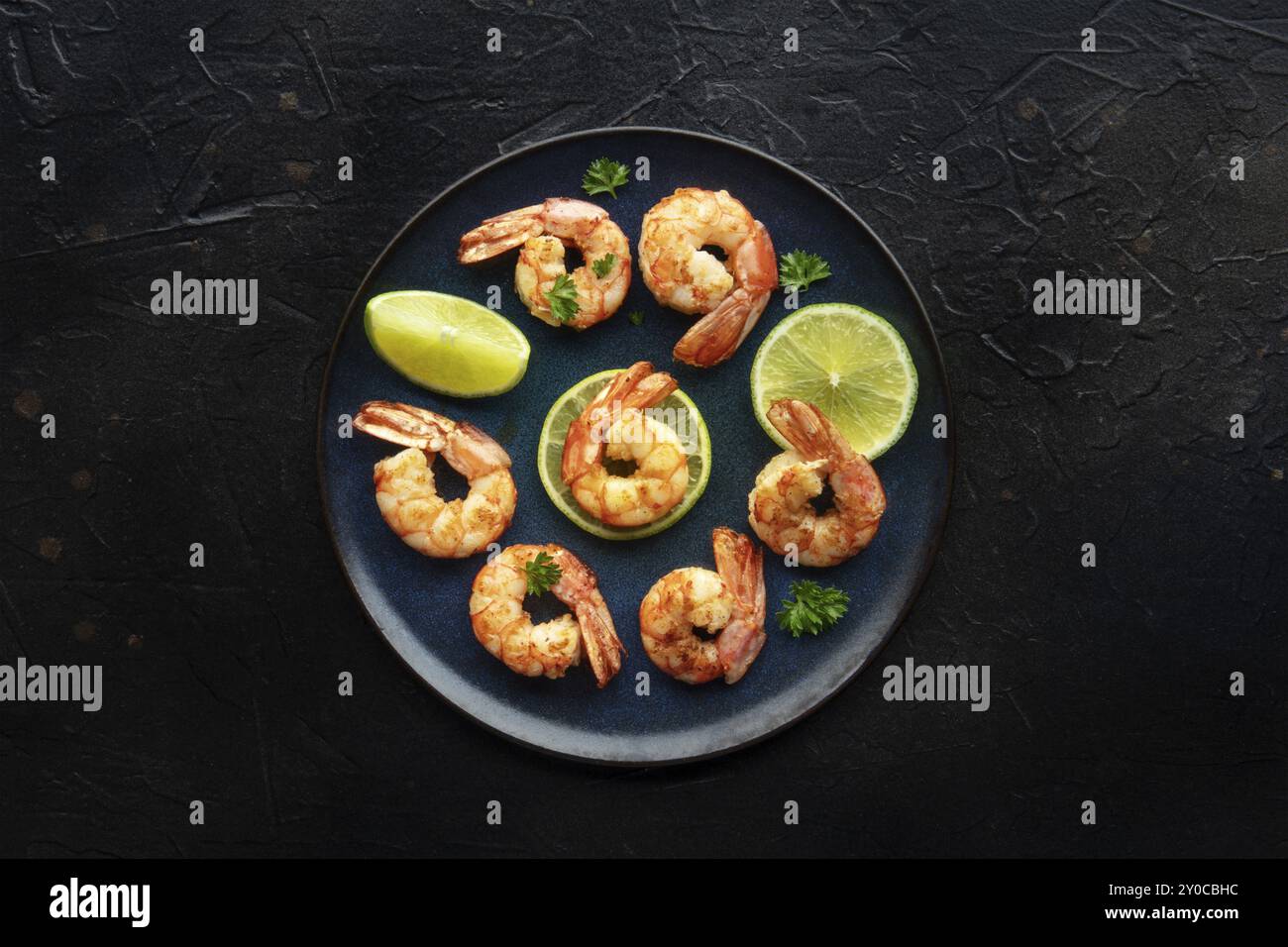 Shrimps, oben flach auf Schwarz geschossen. Gekochte Garnelen mit Limette auf blauem Teller, Gourmet-Vorspeise, Lebensmittelfotografie Stockfoto