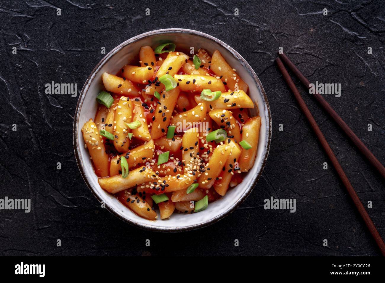 Tteokbokki oder Topokki, koreanisches Streetfood, scharfe Reiskuchen in Gochujang-Sauce aus rotem Pfeffer, von oben mit Stäbchen auf schwarzem Hintergrund geschossen, Fo Stockfoto