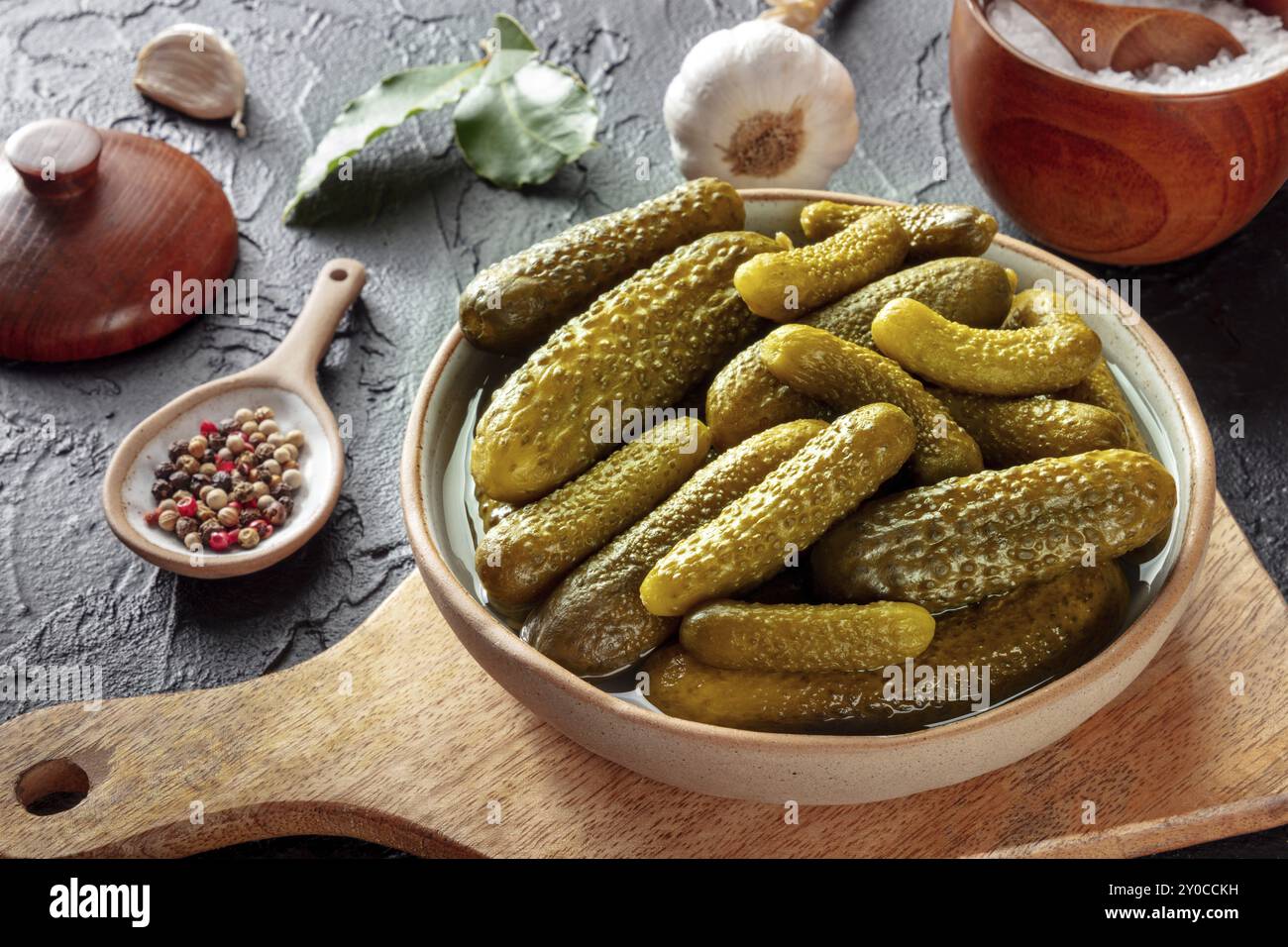 Eingelegte Gurken mit Salz, Pfeffer, Knoblauch und Lorbeerblatt. Fermentierte Lebensmittel. Hausgemachte Dosengurken auf einem dunklen Tisch, Lebensmittelfotografie Stockfoto