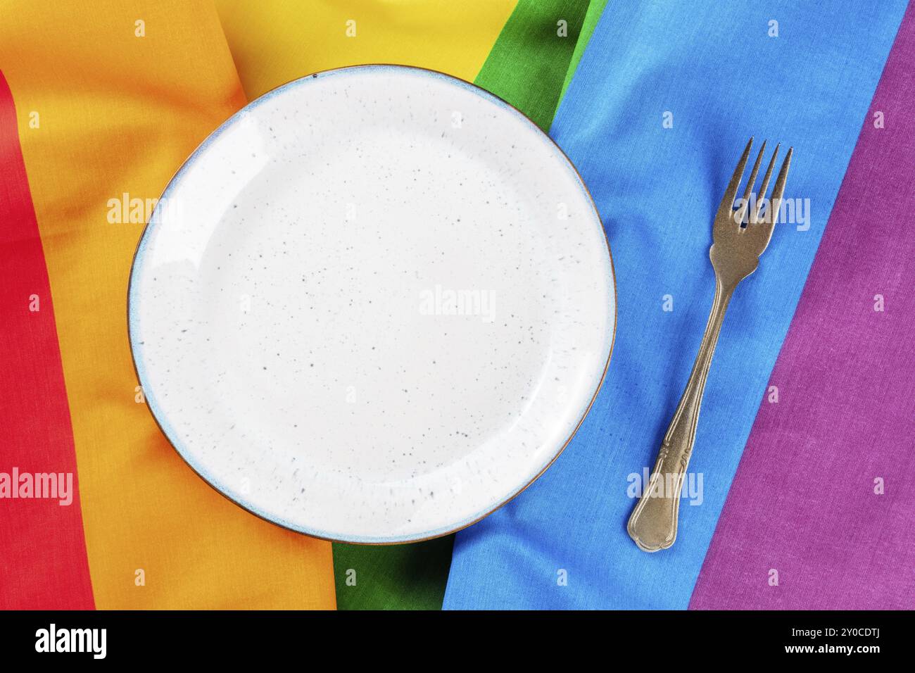 Gay Dinner Konzept. Ein Platz an einem Restauranttisch mit einem Teller und einer Gabel, ein flacher Lay-Shot über der LGBT-Regenbogenfahne, Lebensmittelfotografie, Stockfoto