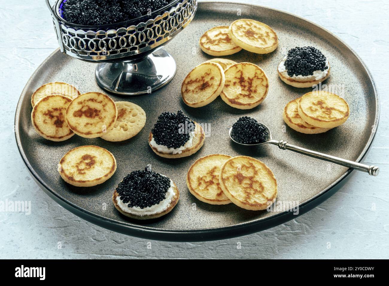 Blinis mit schwarzem Kaviar und Frischkäse, auf festlichem Gericht, Mini-Pfannkuchen, eine elegante Vorspeise Stockfoto