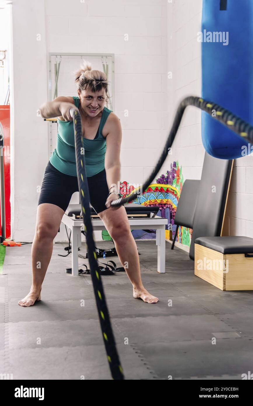 Die Frau versucht ihr Möglichstes in einer Kampfseilübung und demonstriert ihre Hingabe und Entschlossenheit in ihrem körperlichen Training im Fitnessstudio Stockfoto