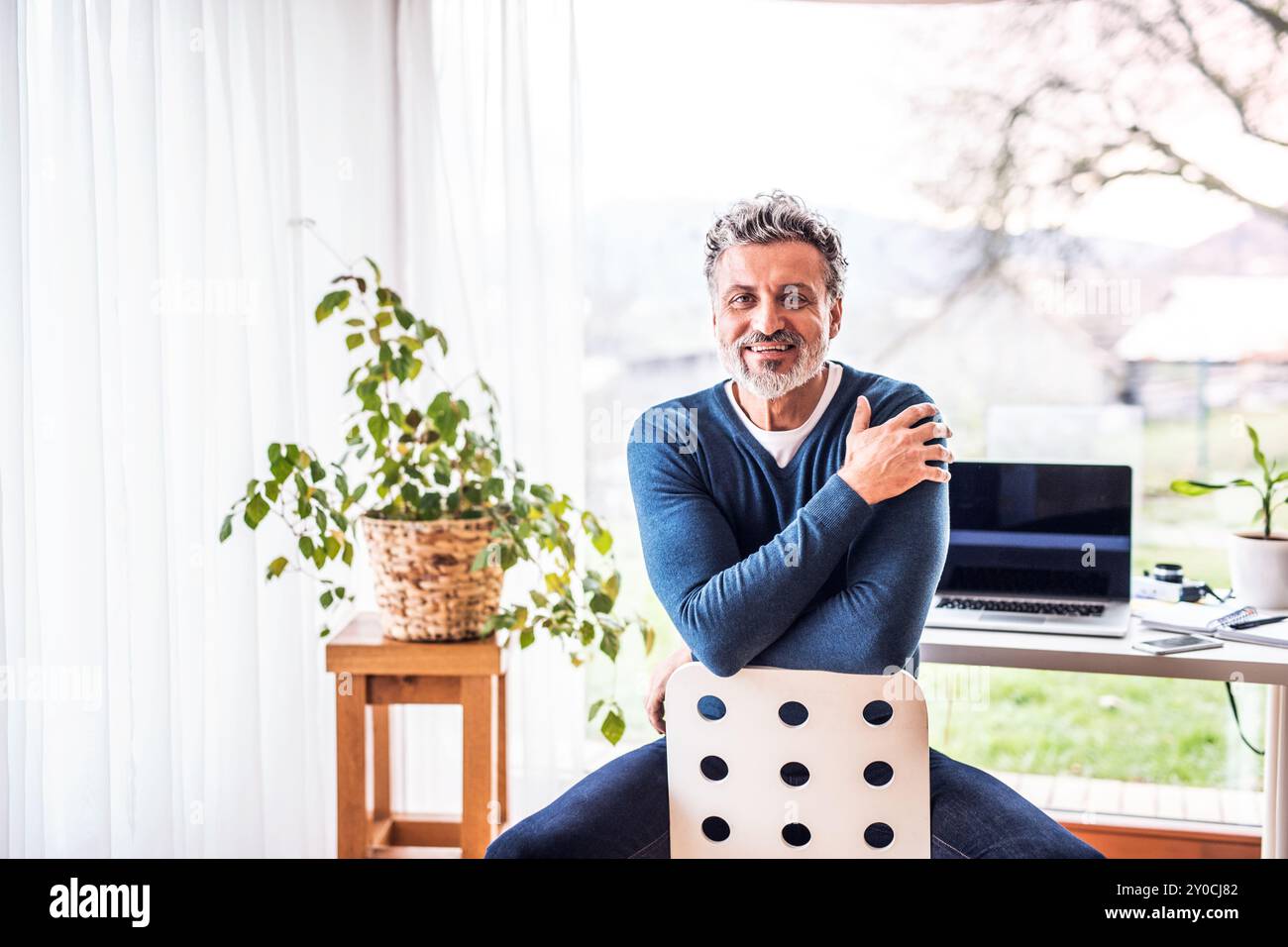 Homeoffice für einen schönen Mann. Mann, der rückwärts auf dem Stuhl sitzt. Telearbeit. Stockfoto
