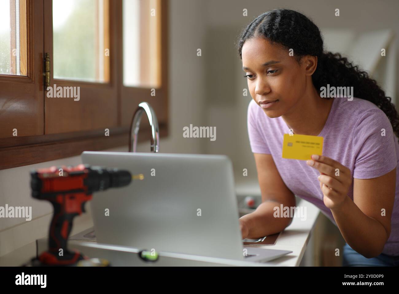 Schwarze Frau, die ein Haus in der Küche restauriert und online mit Laptop und Kreditkarte kauft Stockfoto