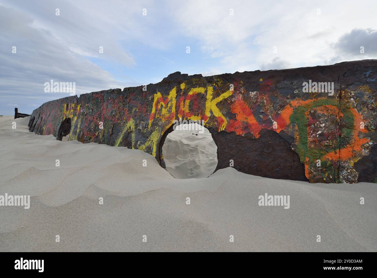Strandszene mit einer Betonkonstruktion, die mit farbenfrohen Graffiti auf Schiffswracks bedeckt ist, teilweise in Sand unter einem bedeckten Himmel vergraben, Norderney, East Frisi Stockfoto