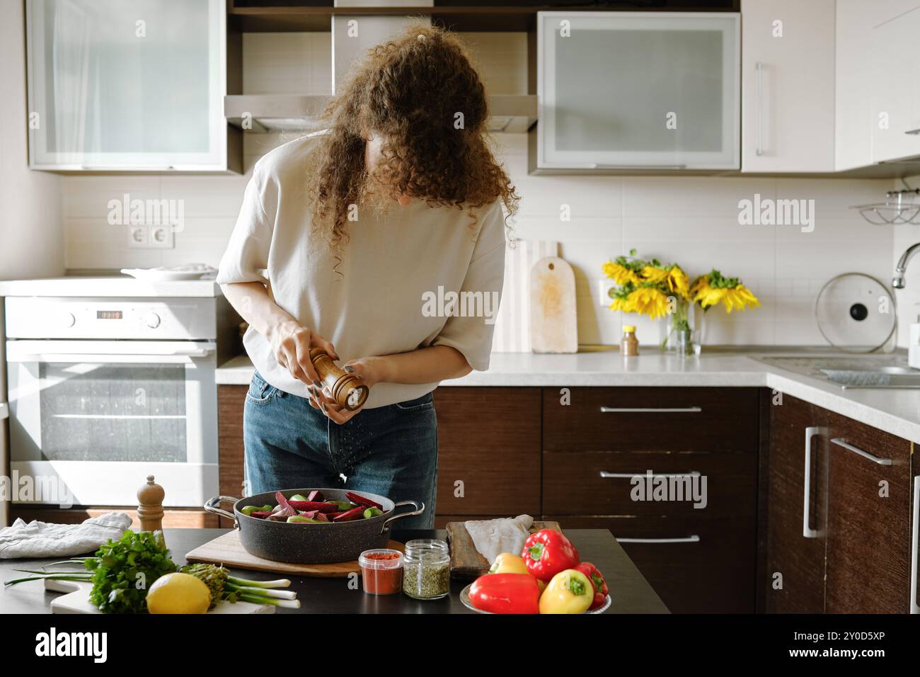 Frau streut Salz aus der manuellen Gewürzmühle auf Gemüse in einer Backform Stockfoto